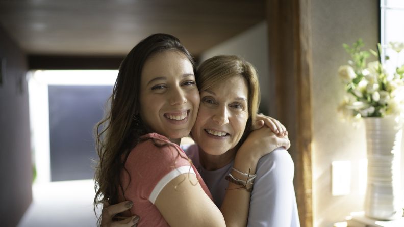 Woman in her early sixties and granddaughter in her thirties, hugging.