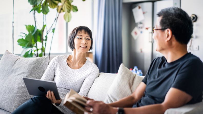 Middle aged Asian couple sitting on a sofa talking