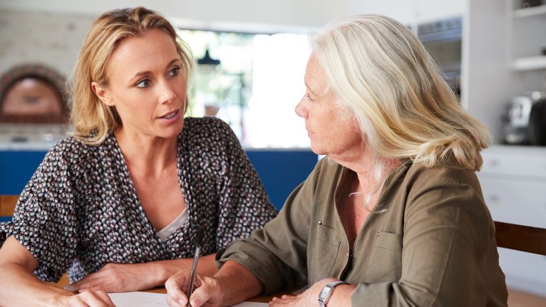 Two women talking. One is in her early forties and the other is in her late fifties. The woman in her late fifties is filling in some paperwork.